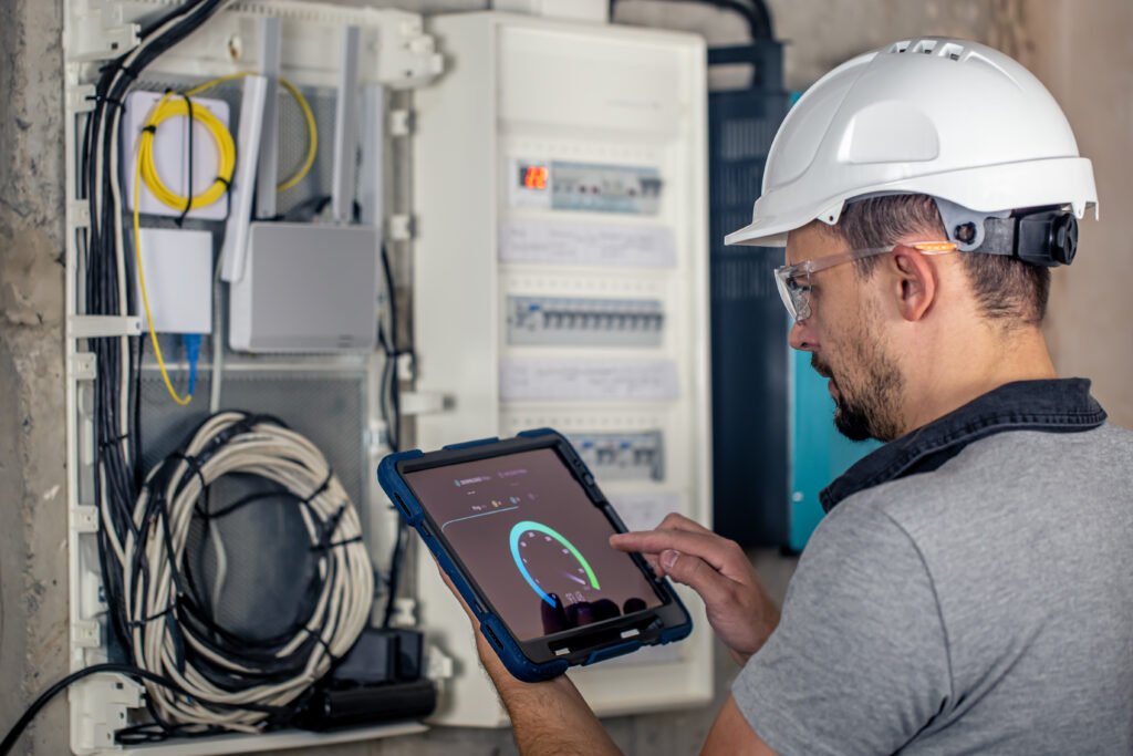 Electrical engineer using a digital tablet to monitor a smart electrical panel and network cabling in a modern building.