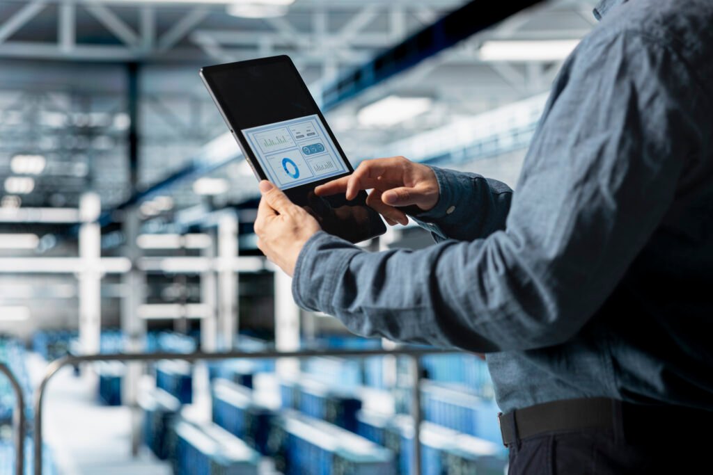 Logistics manager using a tablet to monitor real-time data analytics in a large-scale industrial warehouse.