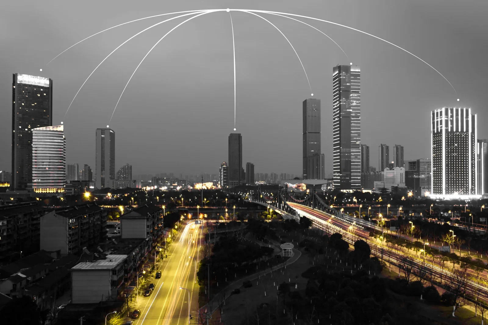 Black and white night skyline of a smart city with glowing light trails representing wireless connectivity and data transfer between skyscrapers and urban infrastructure.